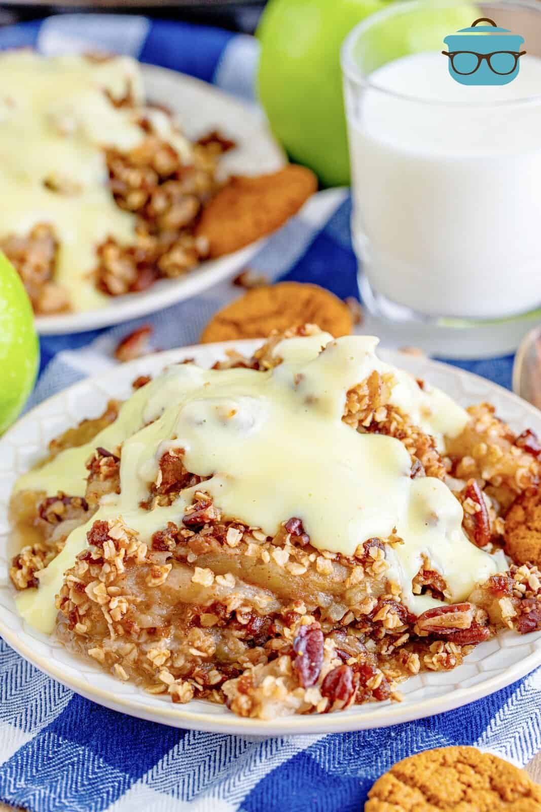 apple crisp on a white plate with vanilla sauce poured onto. 