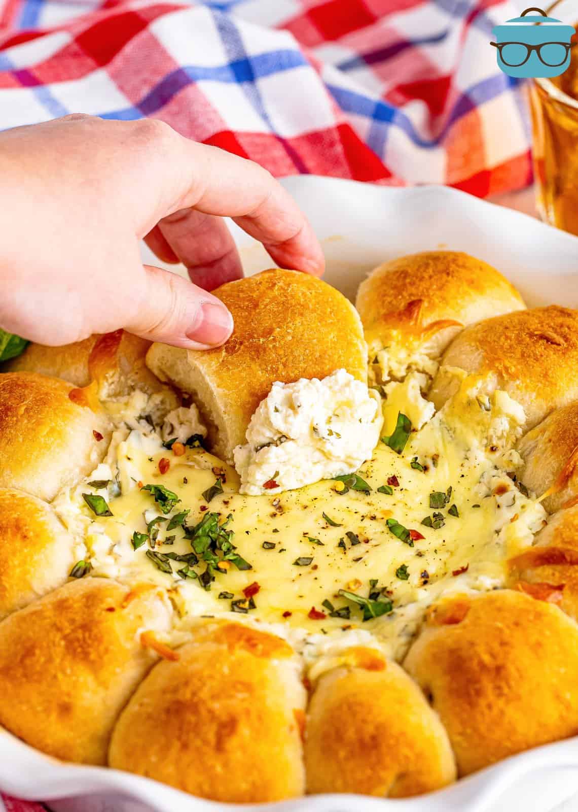a caucasian hand dipping one of the dough balls into the center of the white cheesy dip. 