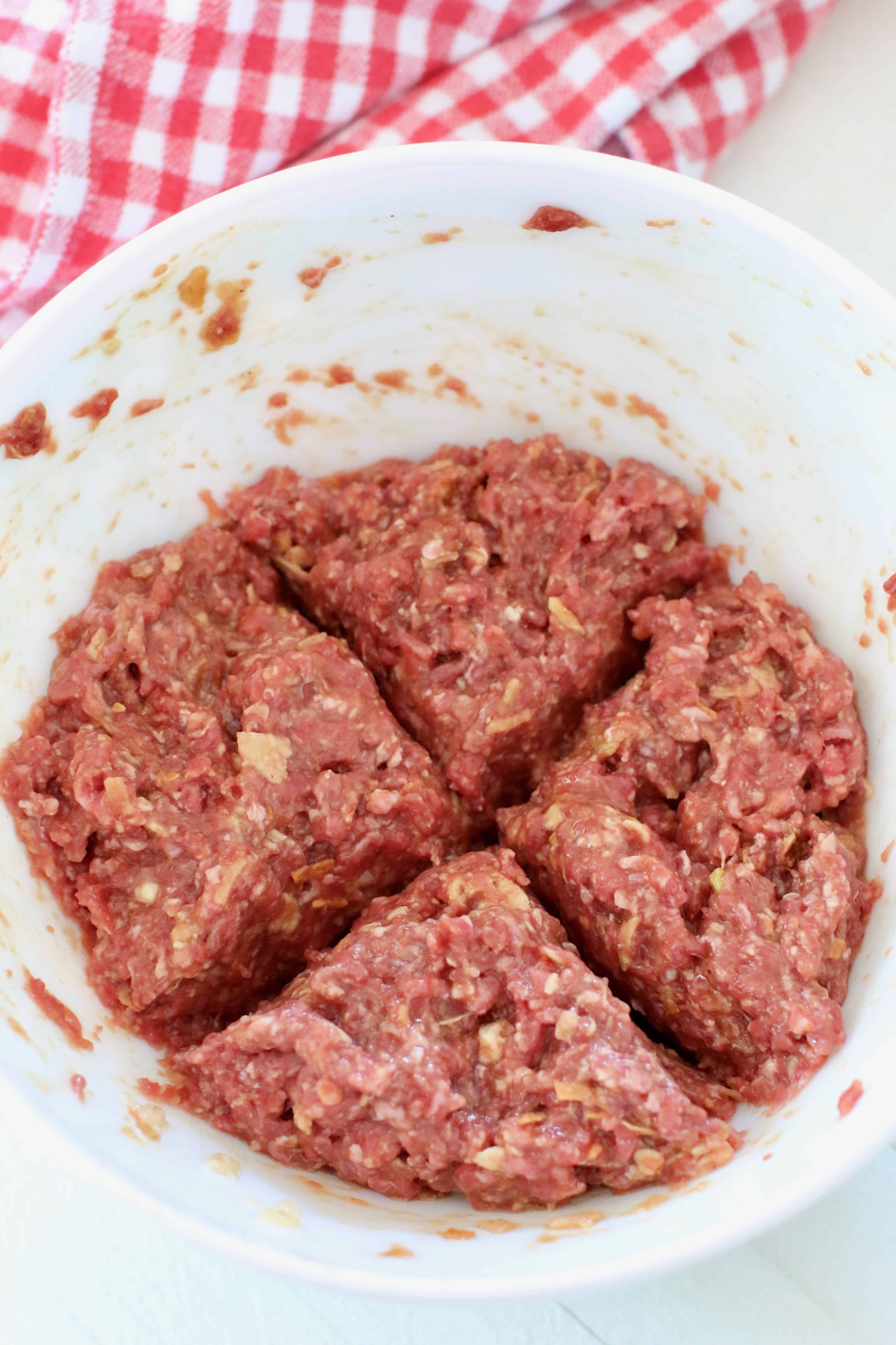 bbq meatloaf mixture divided into four mini meatloafs in a white bowl.