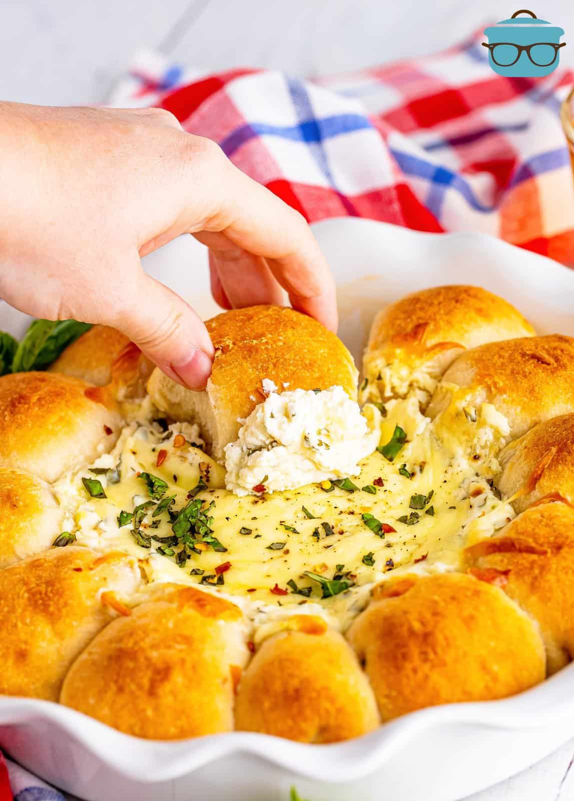 a hand dipping pizza bread ball into the center of the pie dish with the white cheese dip.