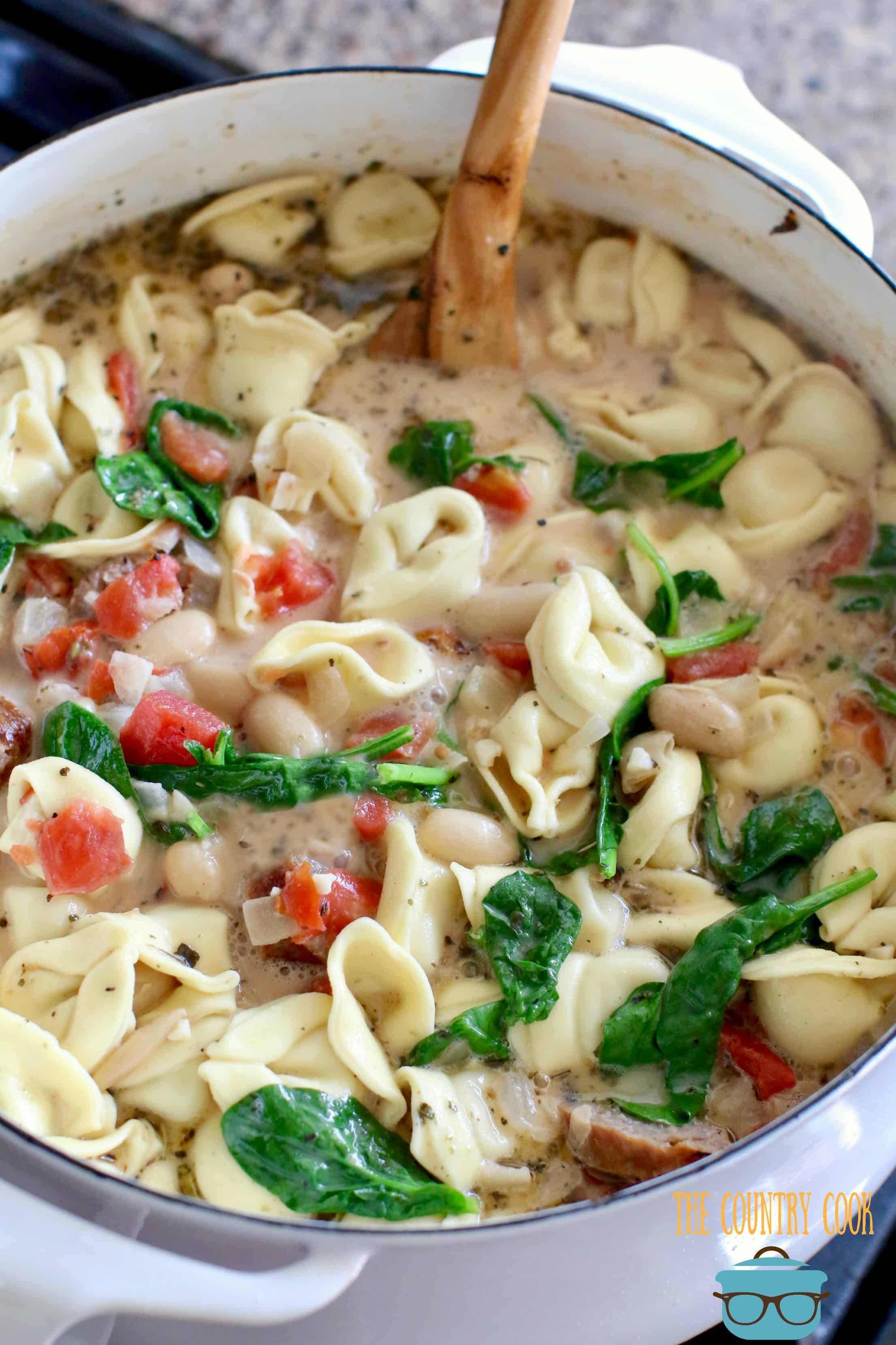 Creamy Tuscan Soup recipe with sausages shown in a white dutch oven.
