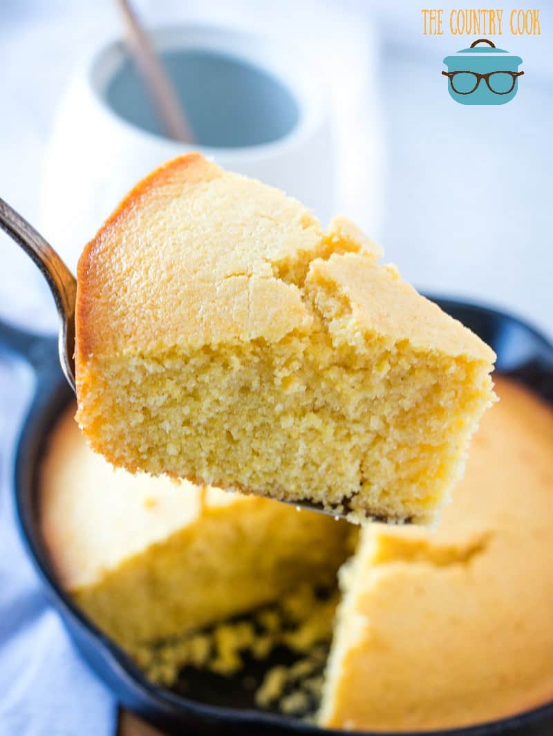 Cornbread baked in a cast iron skillet with a pie spatula scooping out a serving of cornbread.