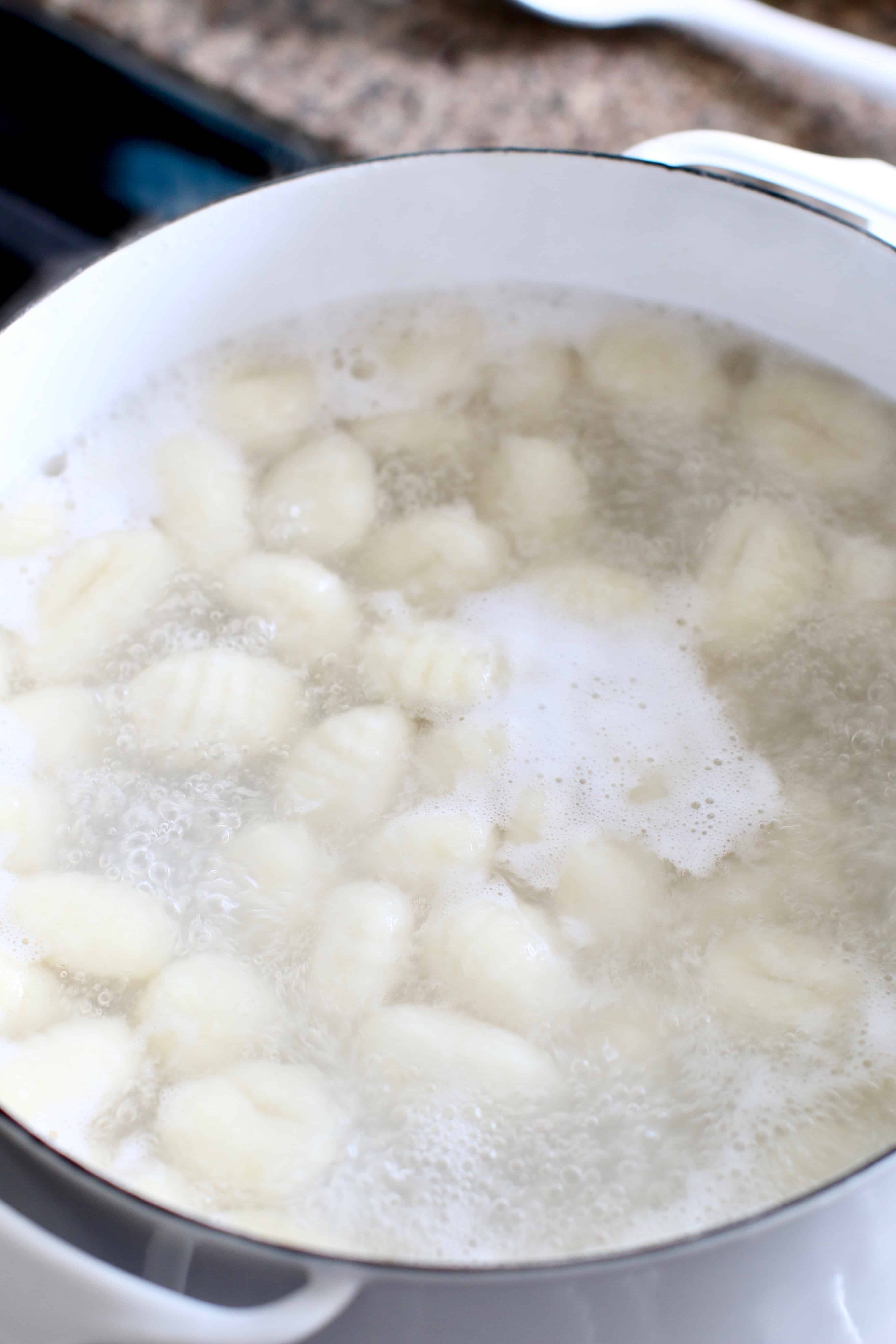 gnocchi boiling in water in a white pot.