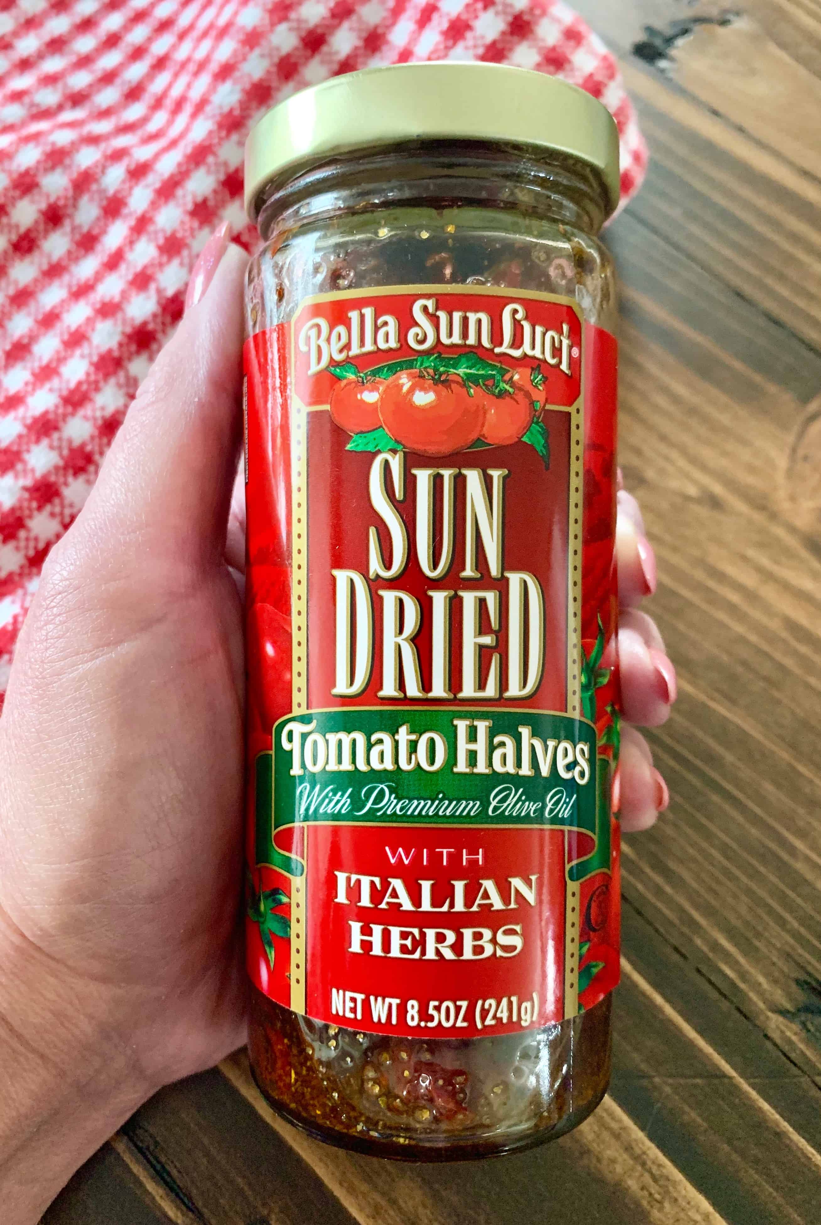 sun-dried tomatoes packed in oil with Italian herbs jar being held by a hand. 