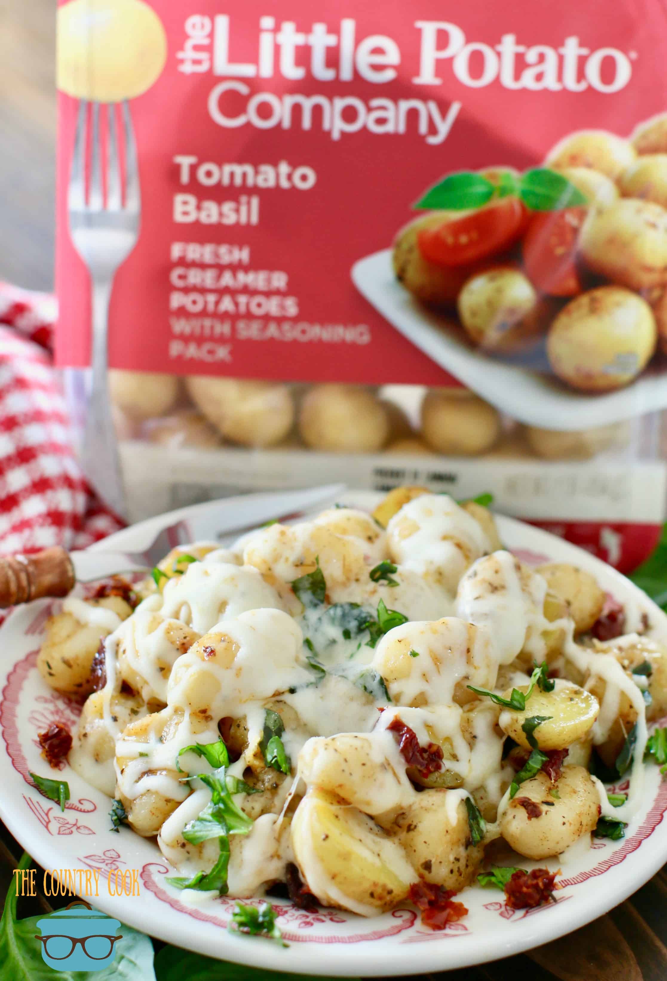 Cheesy Italian Potatoes and Gnocchi with sun-dried tomatoes and fresh basil shown on a plate with a packaging of Little Potatoes in the background.