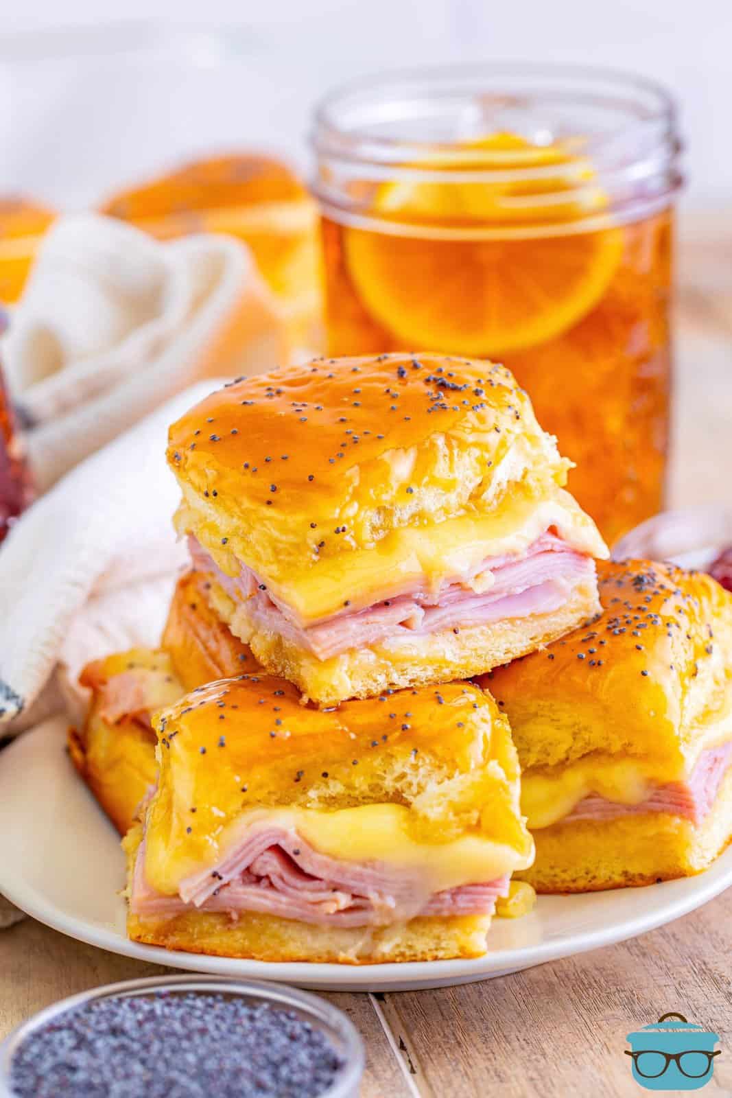 a stack of three glazed ham and cheese sliders on a white plate. 