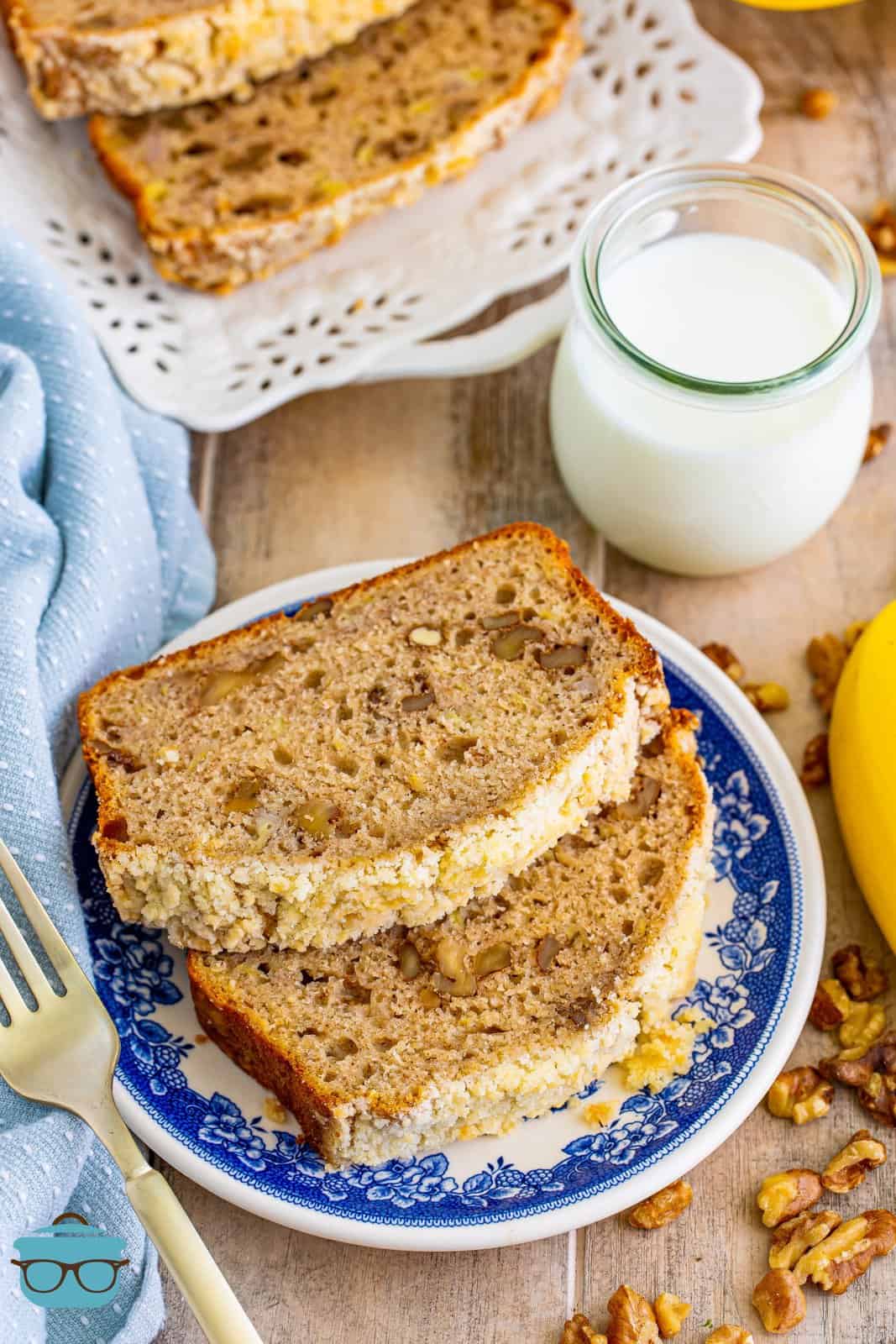 overhead photo of two slices of banana bread on a blue and white plate with a glass of milk in the background.