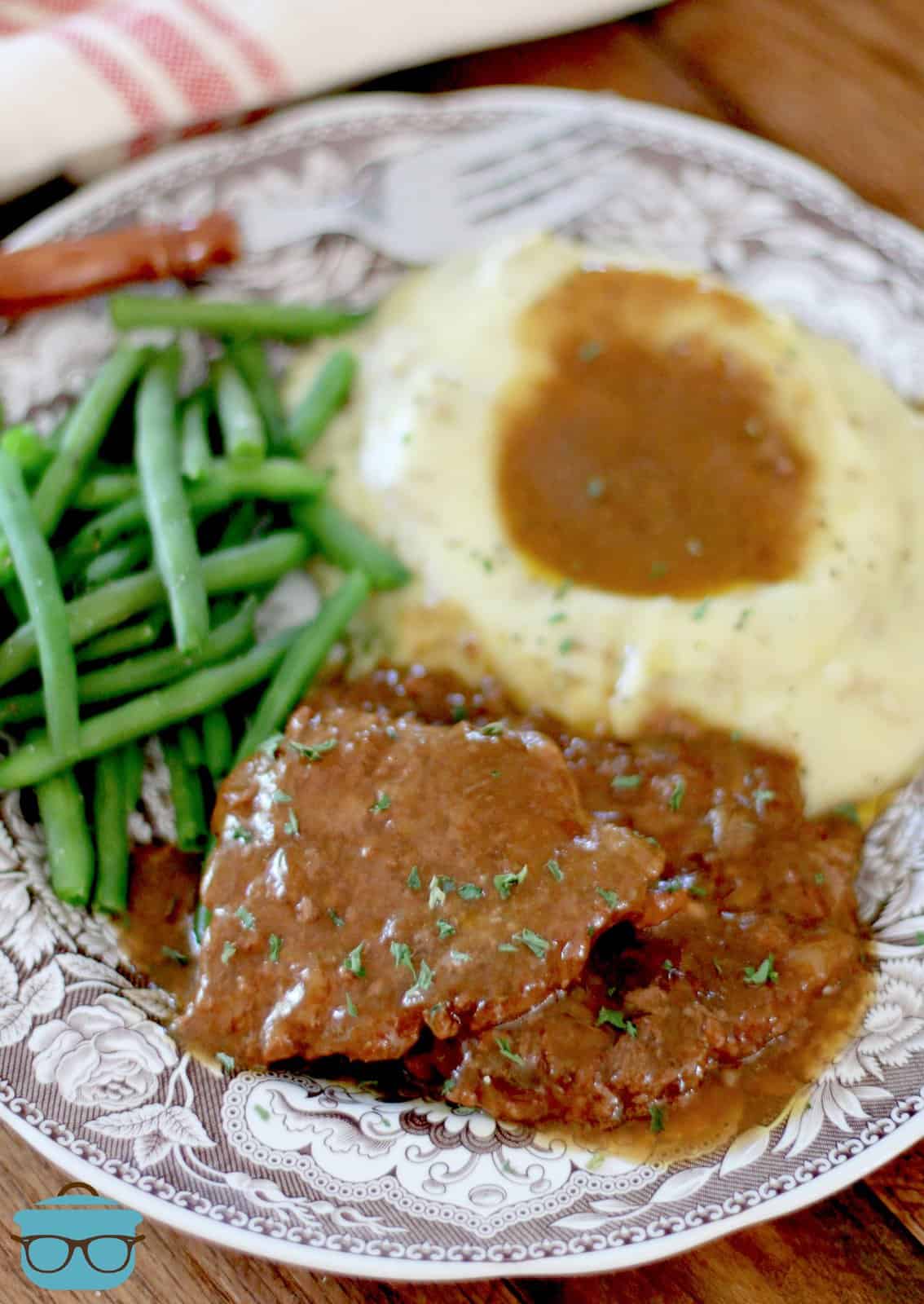cooked cube steaks topped with gravy on a plate with mashed potatoes and cooked green beans.