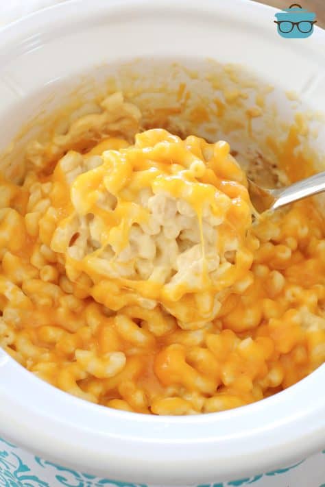 a spoon scooping up a serving of macaroni and cheese out of the slow cooker.