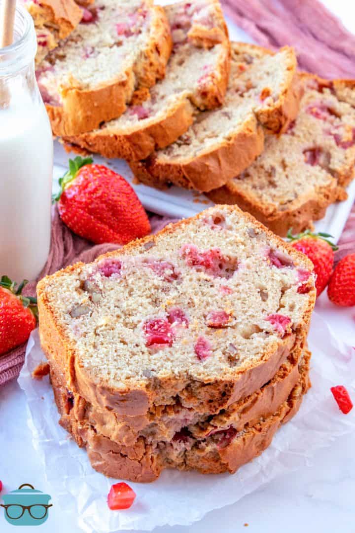 a stack of three slices of strawberry bread laid in front of more slices of strawberry bread laid out on a platter. 