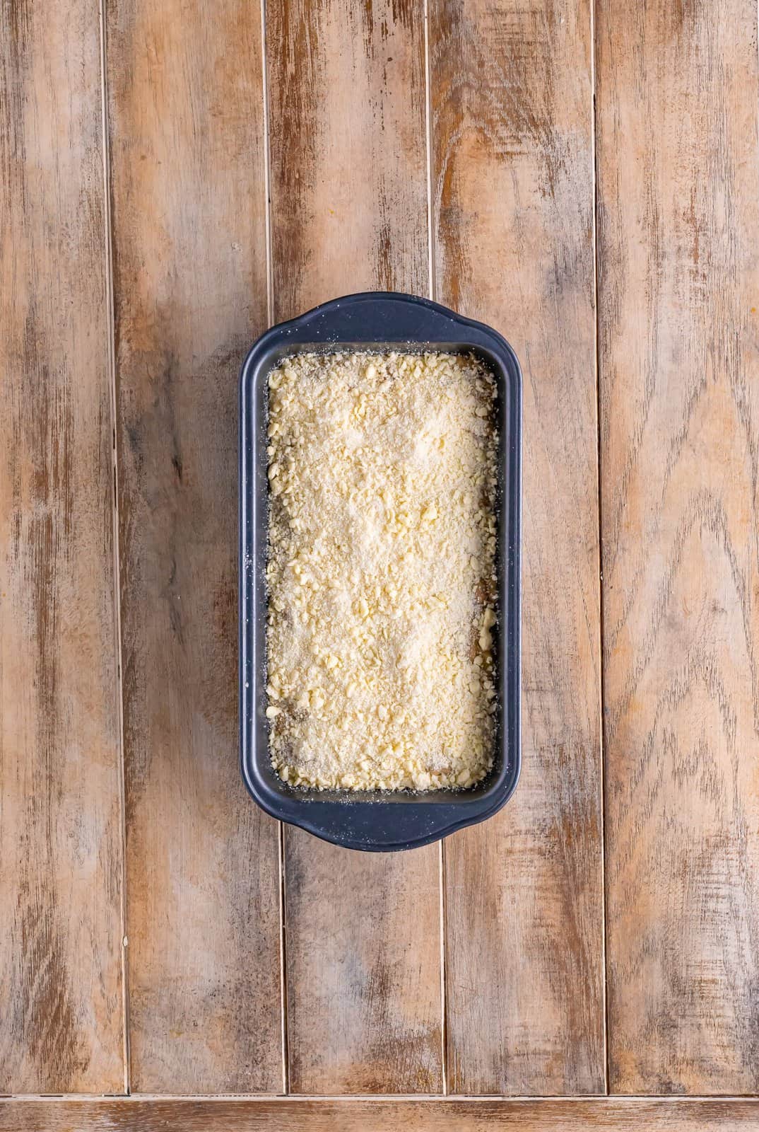 crumble topping shown sprinkled evenly on top of banana bread batter in a loaf pan.