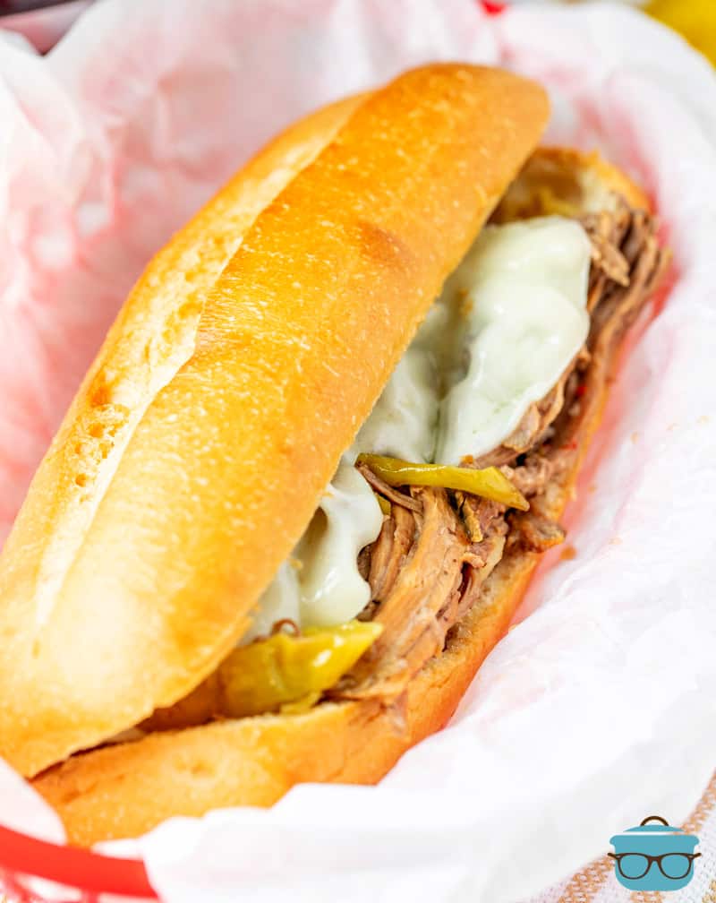 an Italian Beef Sandwich with melted cheese shown in a basket topped with parchment paper. 