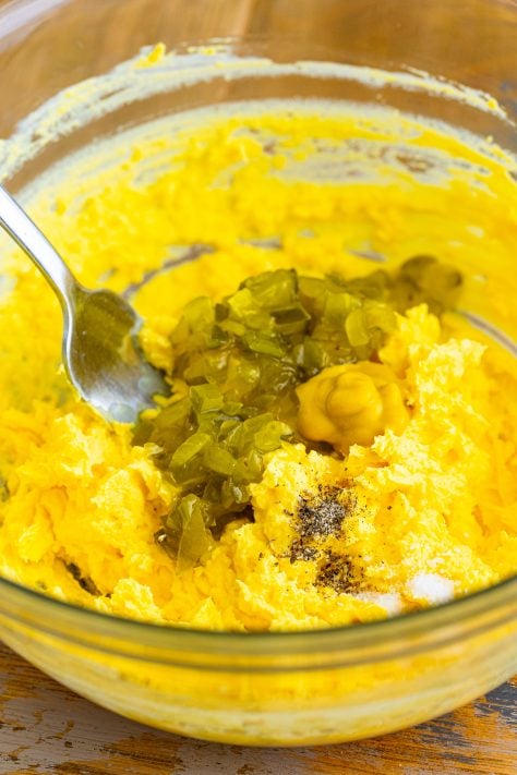 relish, mustard, salt and pepper added to yolk mixture in a bowl.