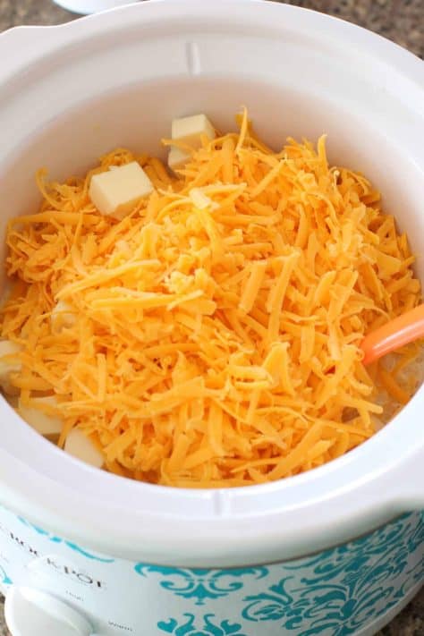 shredded cheeses on top of macaroni noodles in crock pot.