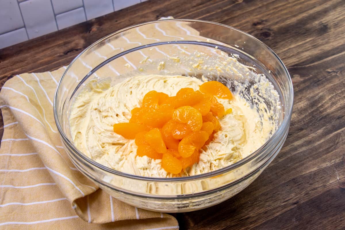 drained mandarin oranges added to cake batter in a bowl.