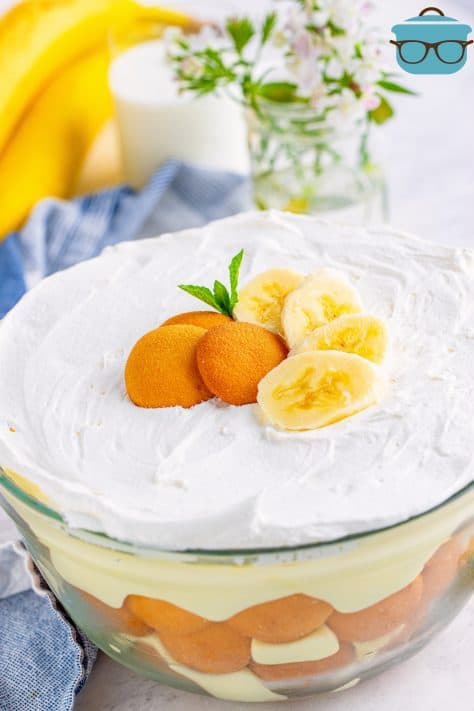 layers of banana pudding shown in a large glass serving bowl with a bunch of bananas in the background