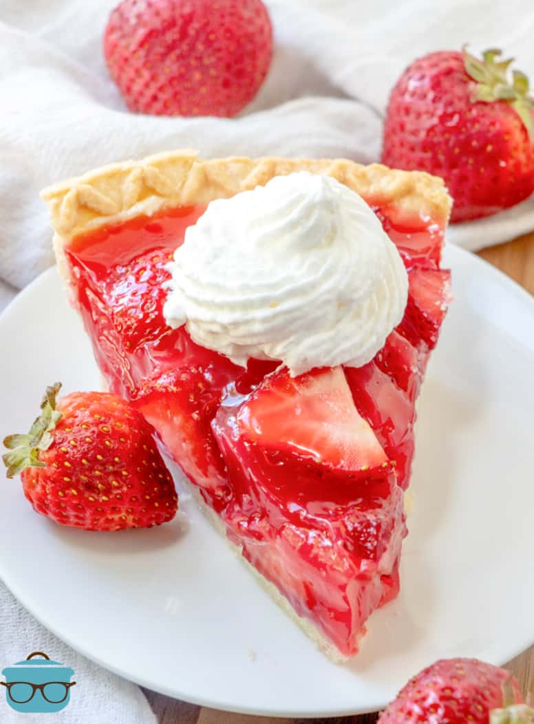 slice of fresh strawberry pie on a wound white plate and a dollop of fresh whipped cream on top.