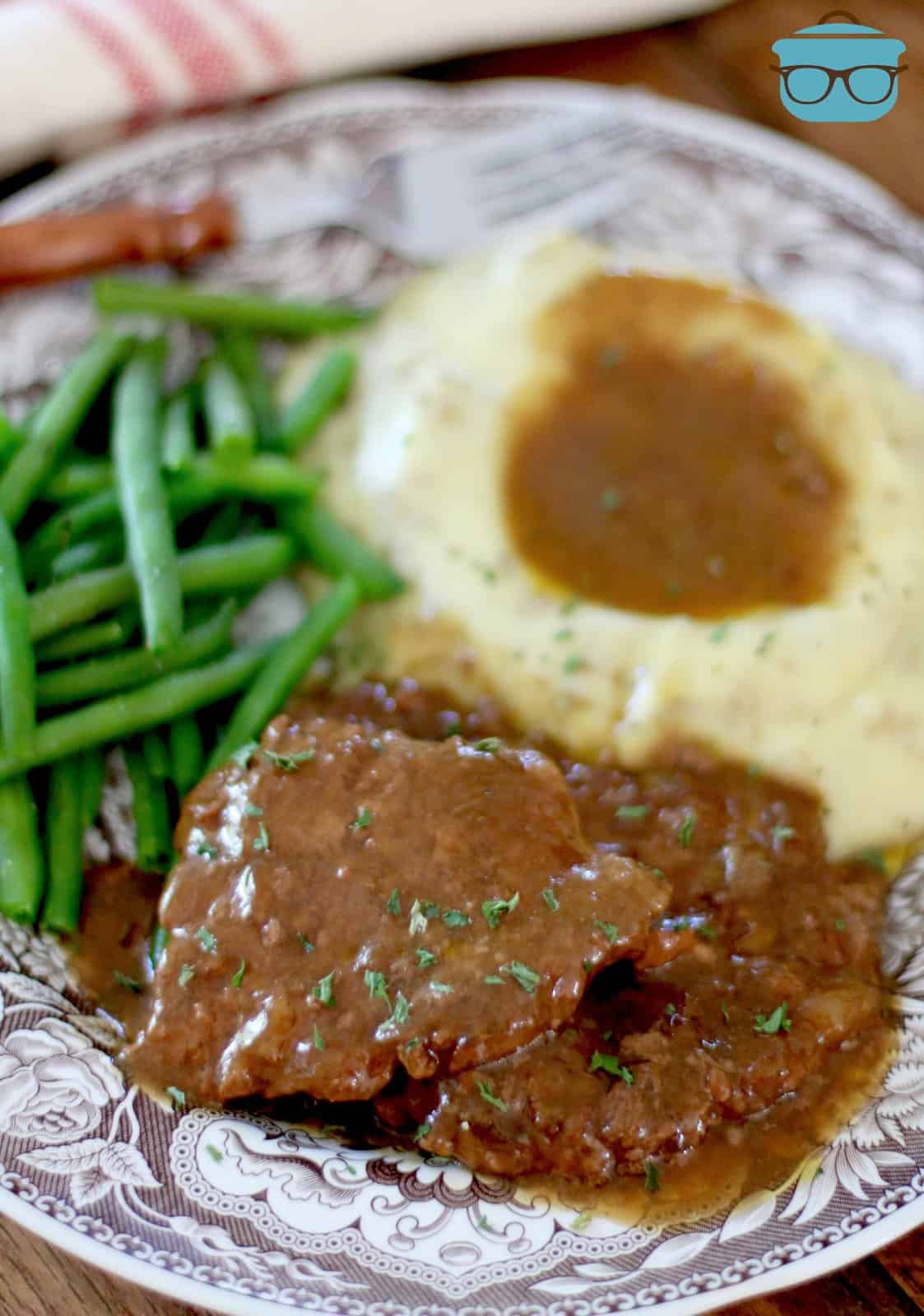 cube steak shown served on a plate with mashed potatoes and green beans.