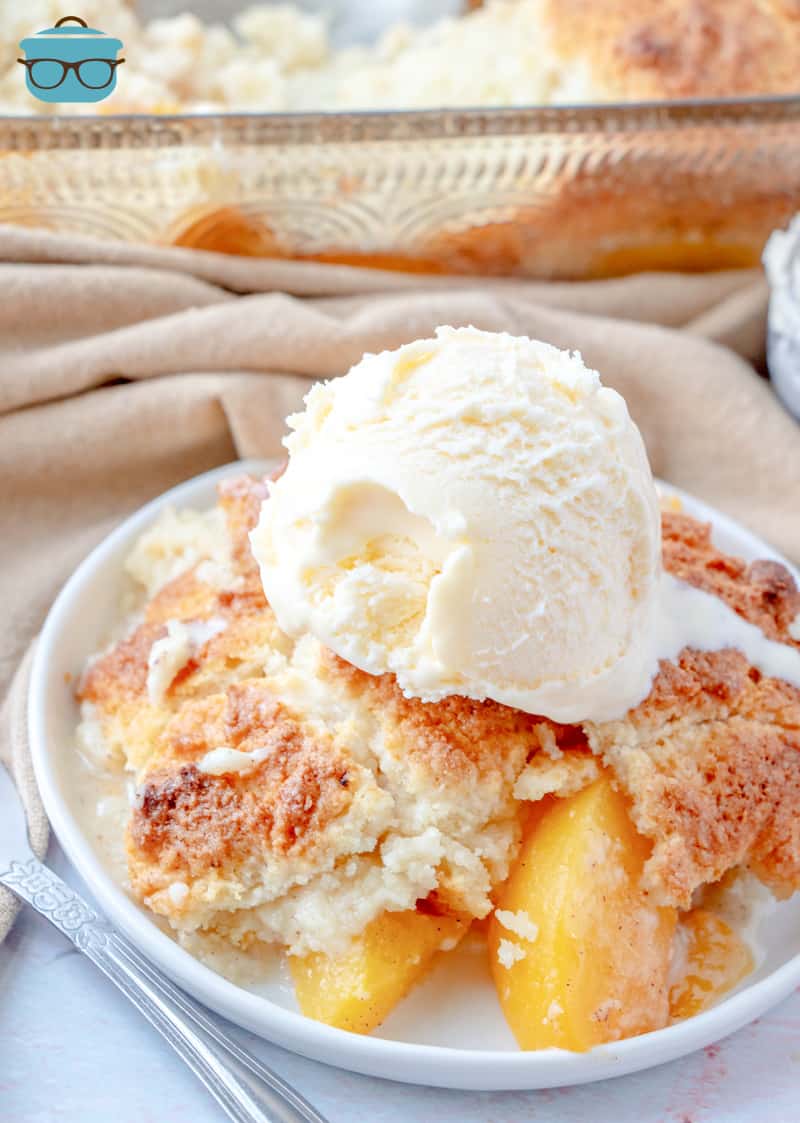 overhead photo of a serving of peach cobbler topped with a scoop of vanilla ice cream on a round white plate. 