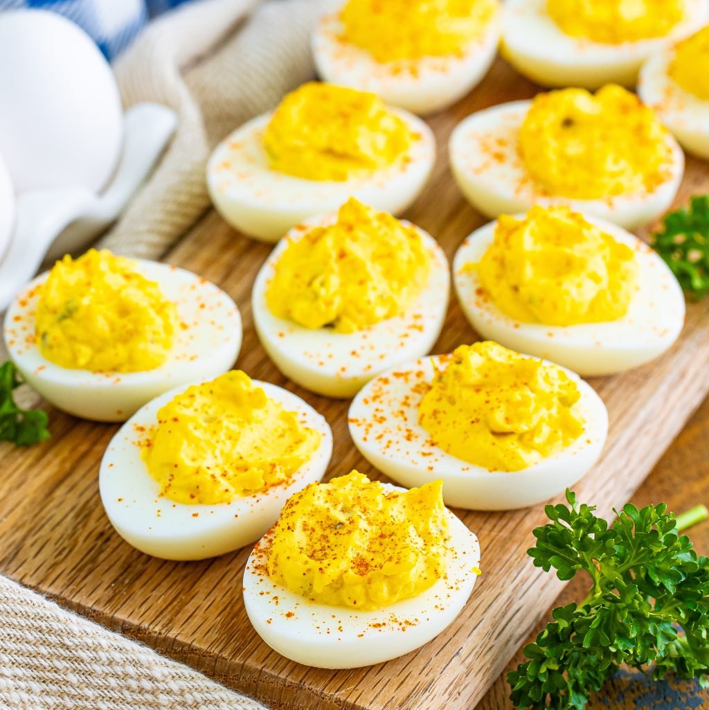 The best deviled eggs shown close up on a wooden board with parsley on the side.