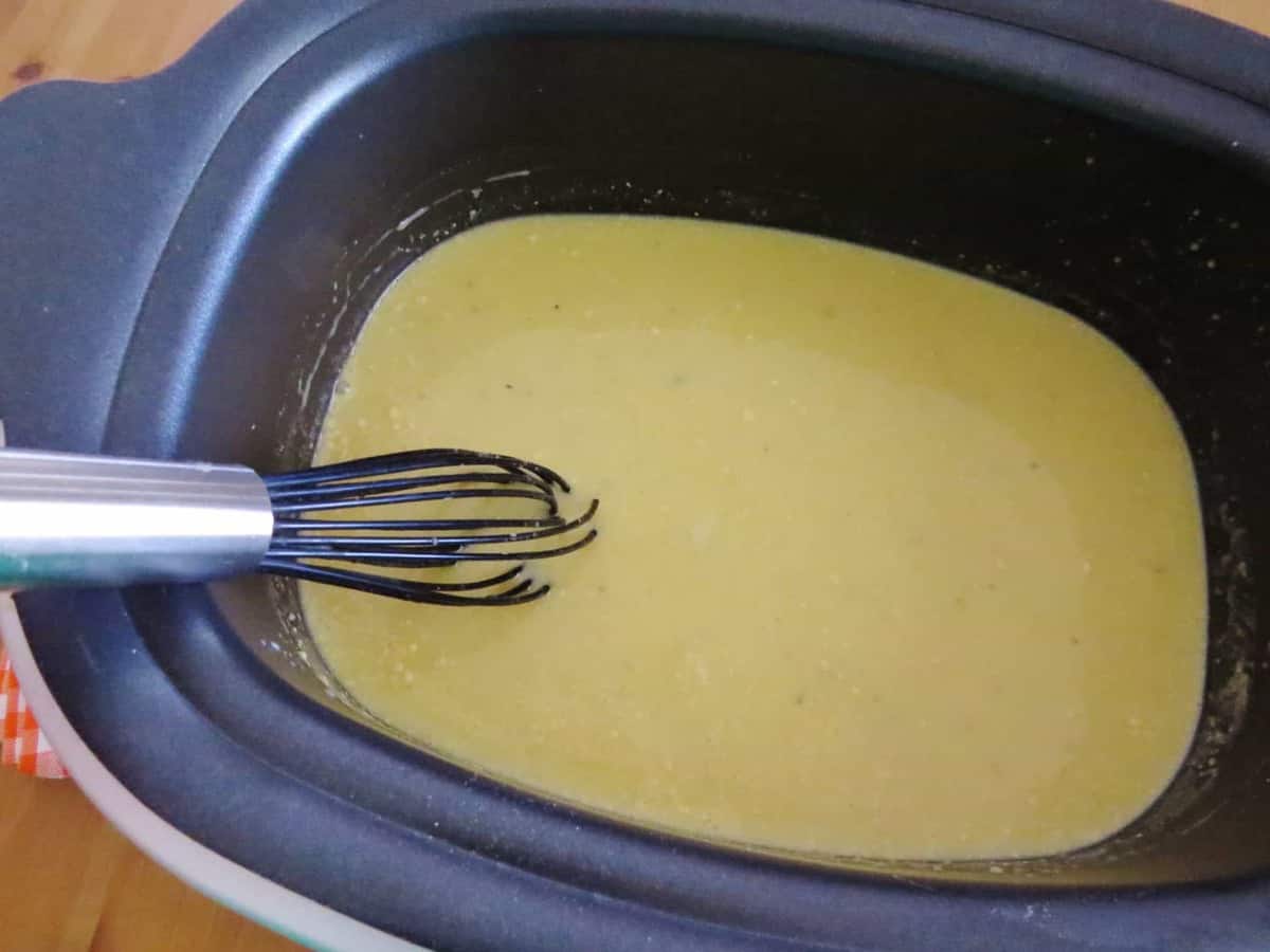 cream of chicken soup with gravy seasoning and water in a slow cooker with a whisk.