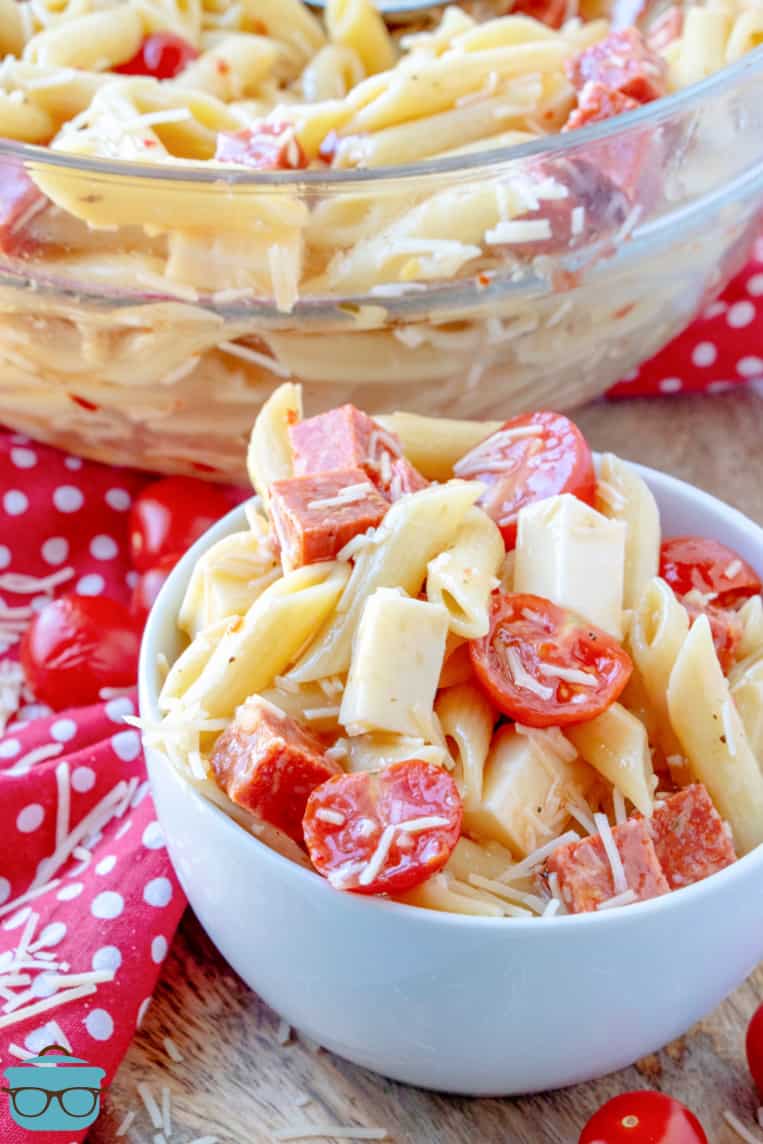 white bowl filled pepperoni pizza pasta salad with a red and white polka dot kitchen towel on the side. 