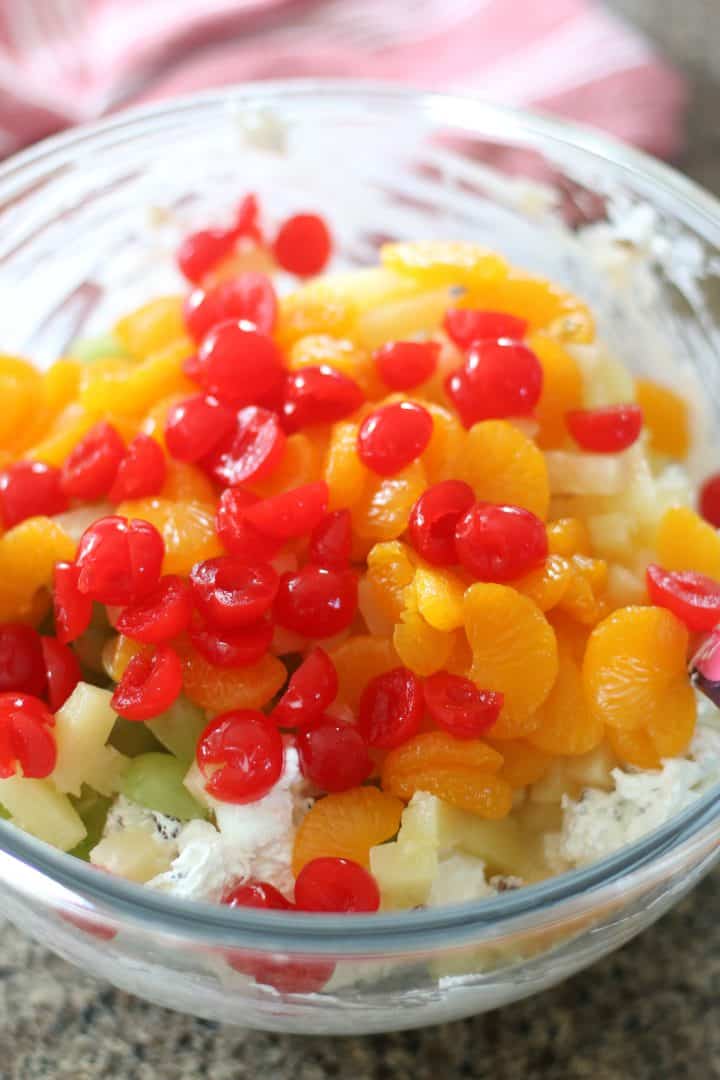 mandarin orange slices, sliced maraschino cherries, pineapple tidbits and sliced green grapes added to a large clear bowl with cool whip.