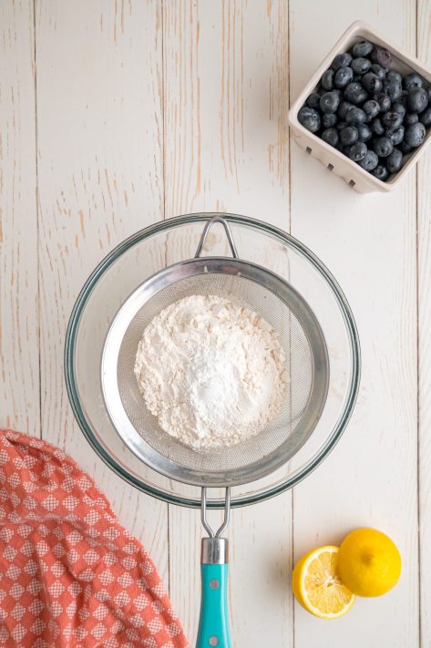 A bowl with a sifter sifting baking powder, salt, and flour.