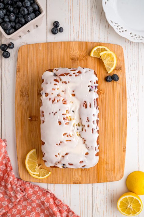 A glazed Blueberry Lemon bread loaf on a wooden board.