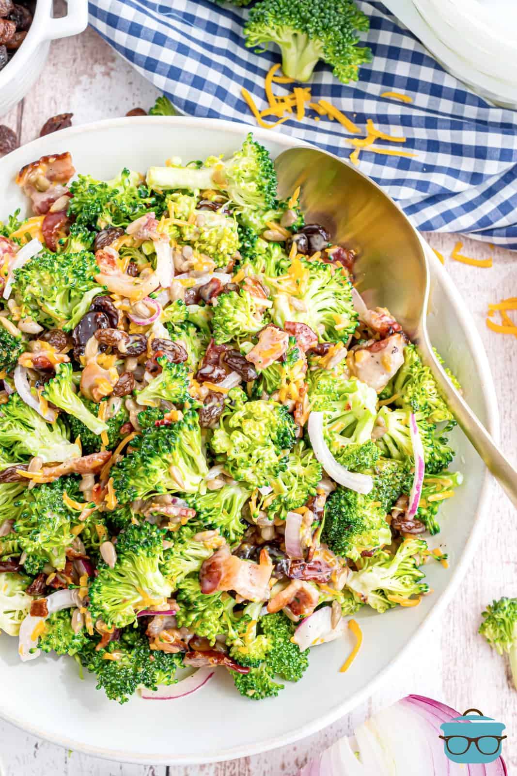 fully combined broccoli salad in a shallow white bowl with a silver spoon inserted into the salad. 