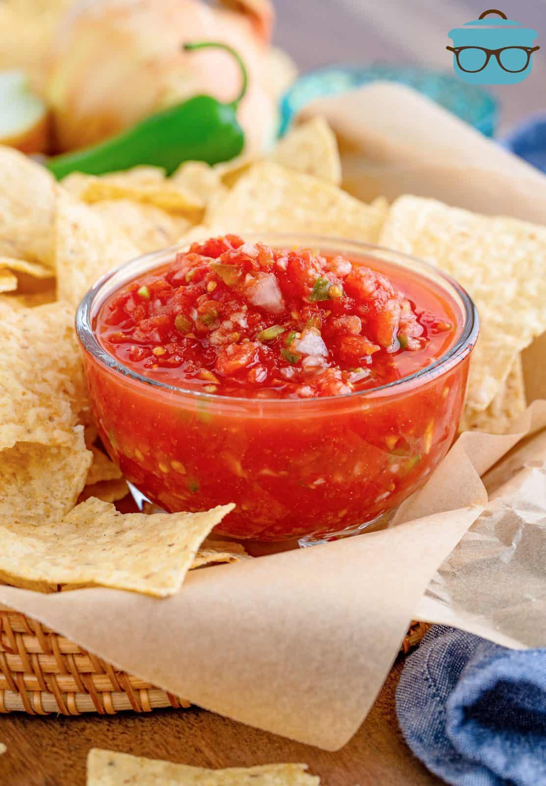 small, clear bowl of salsa in a basket with tortilla chips.