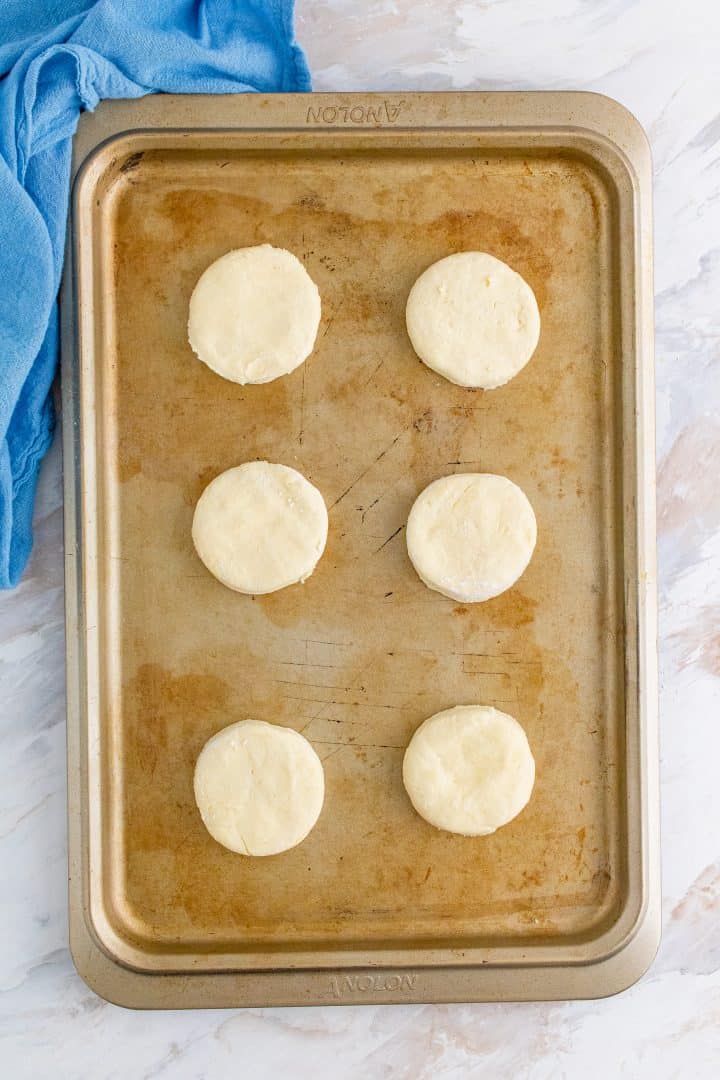 six round biscuit dough circles shown on a cookie sheet.