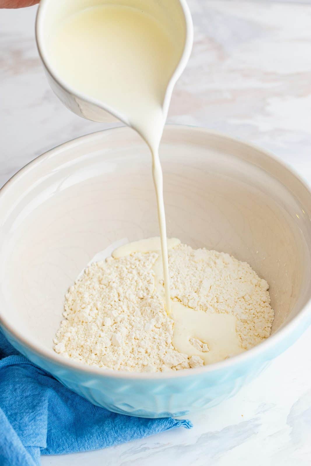 pouring heavy cream into white bowl that has self-rising flour in it.