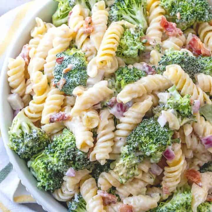 Creamy Bacon Broccoli Pasta Salad in a large white serving bowl surrounded by a white and yellow dish towel