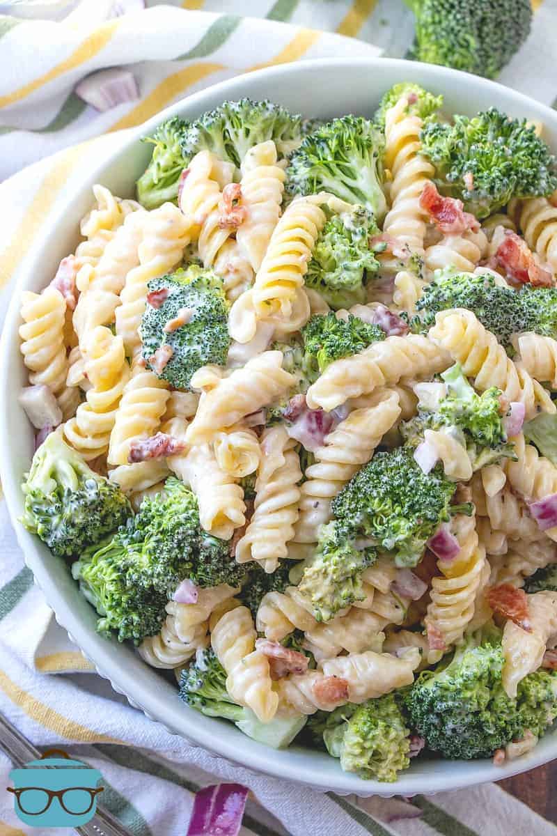 Creamy Bacon Broccoli Pasta Salad in a large white serving bowl surrounded by a white and yellow dish towel.