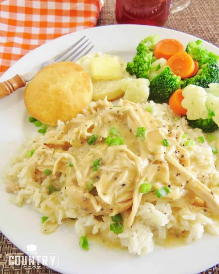 shredded chicken and gravy served over cooked rice on a white plate with a fork.
