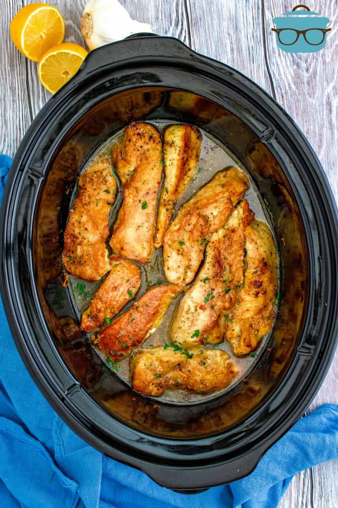 fully cooked lemon garlic chicken in an oval black slow cooker.