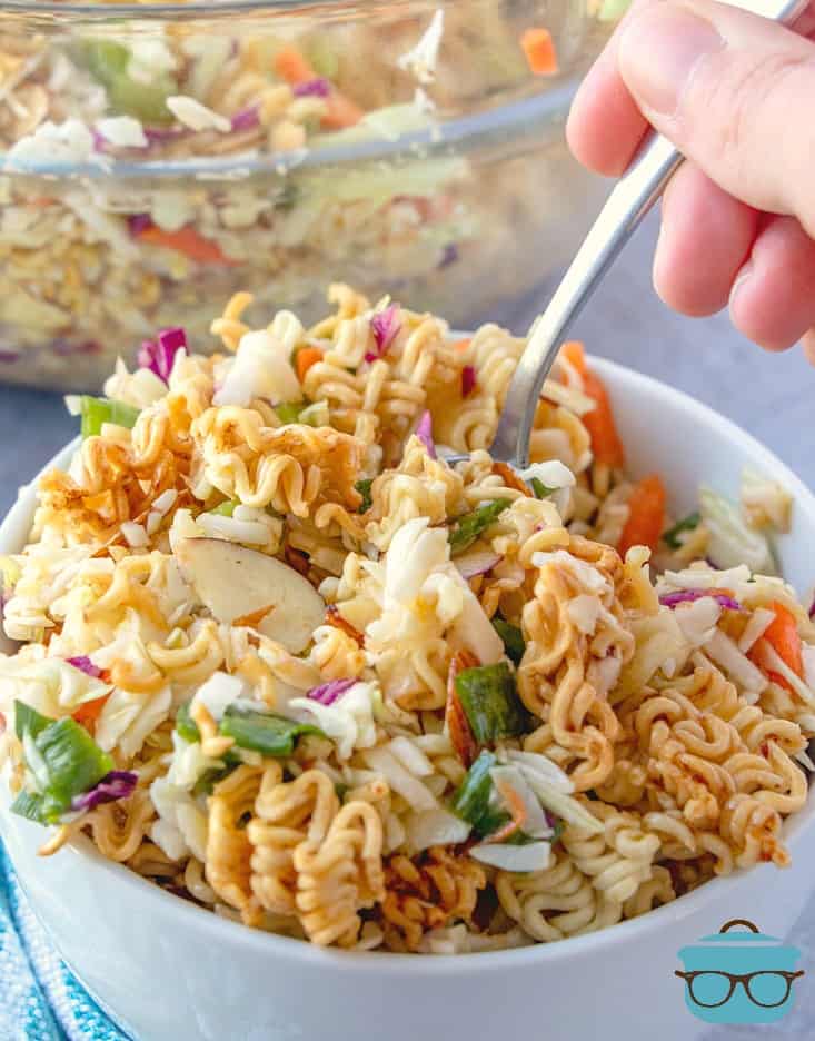 a spoon being inserted into the Ramen Noodle Salad that is in a white bowl.