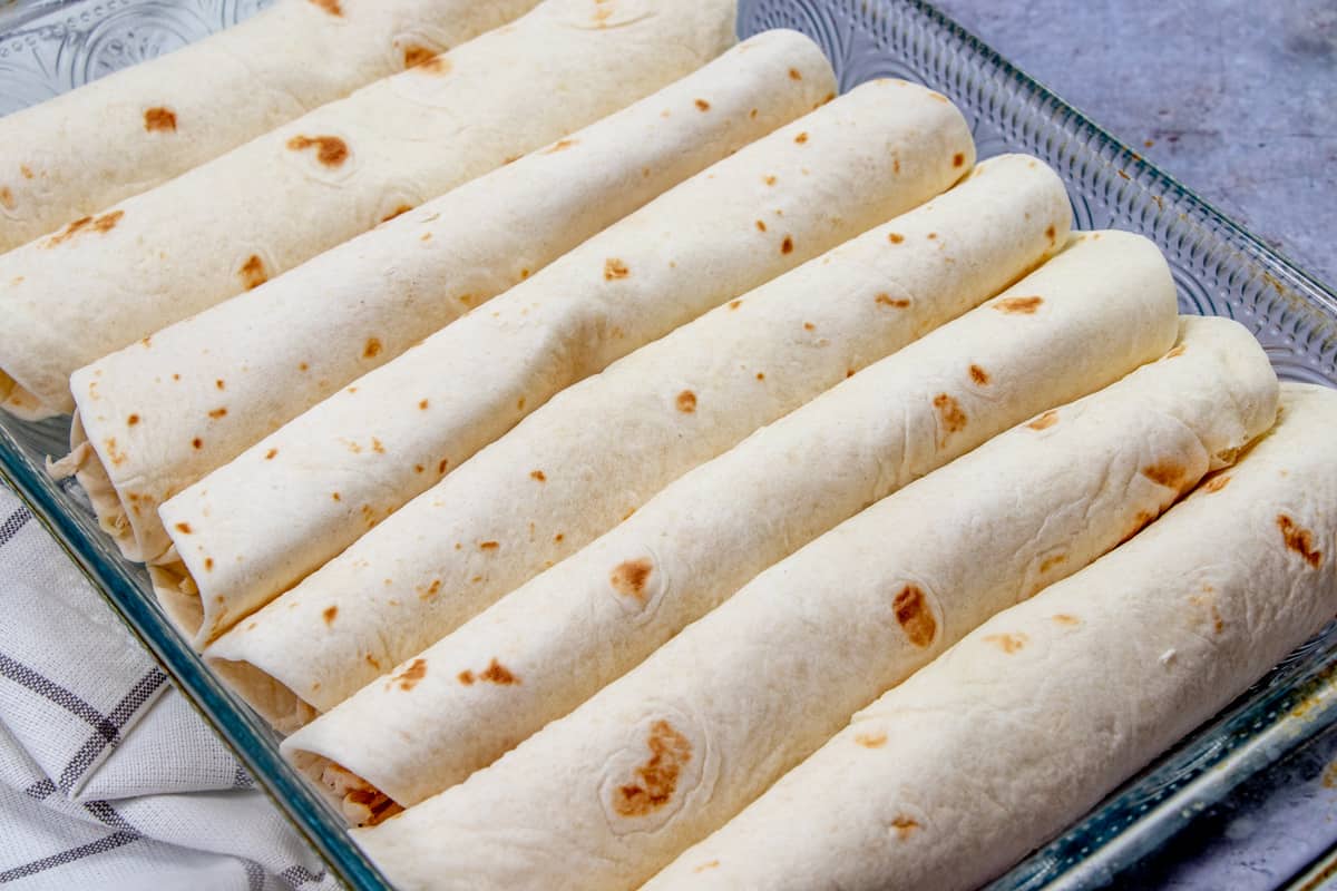chicken filled flour tortillas rolled up and placed into a glass baking dish