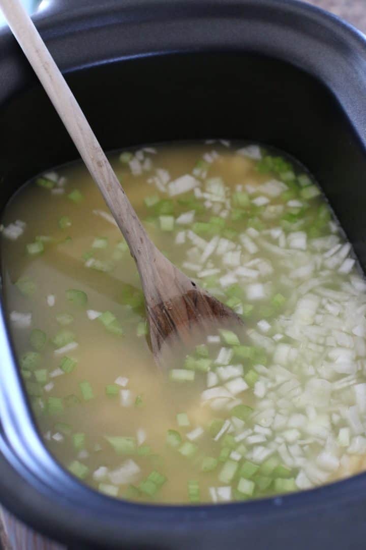 chicken broth, diced onions and celery and cream of chicken soup in a slow cooker with a wooden spoon