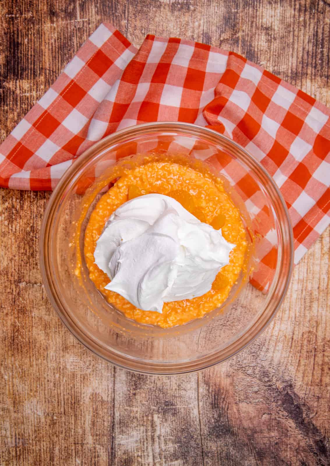 cool whip whipped topping shown dolloped on top of orange gelatin mixture in a clear glass bowl.
