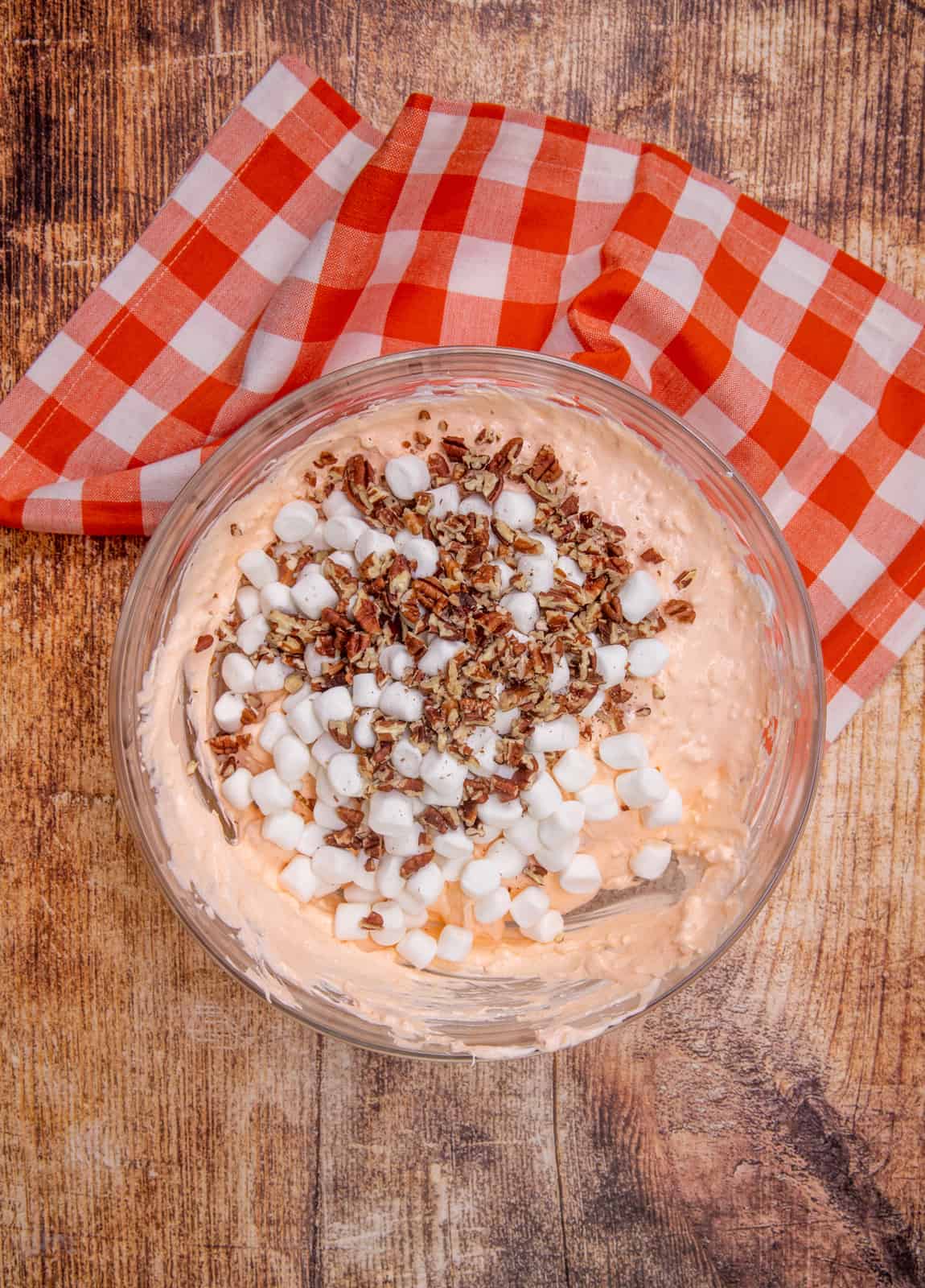 mini marshmallows and chopped pecans added to orange gelatin mixture in a large clear bowl.