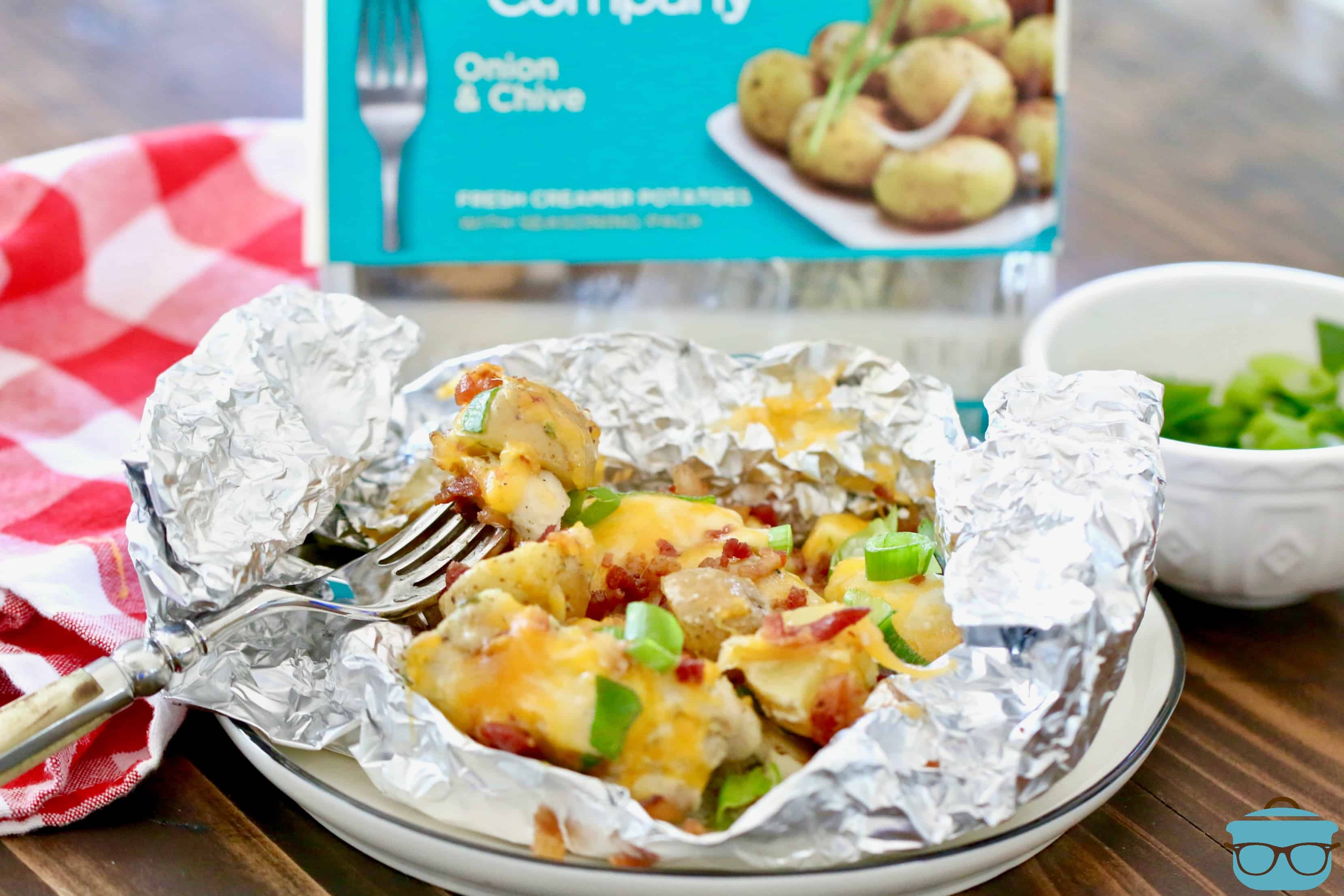 foil packet of chicken and potatoes on a plate with a fork to the side. 
