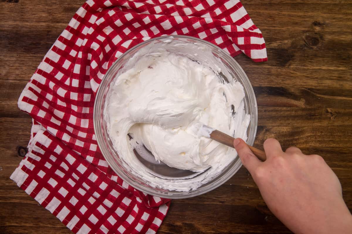 powdered sugar and cream cheese mixed together in a large clear bowl with a large wooden spoon.
