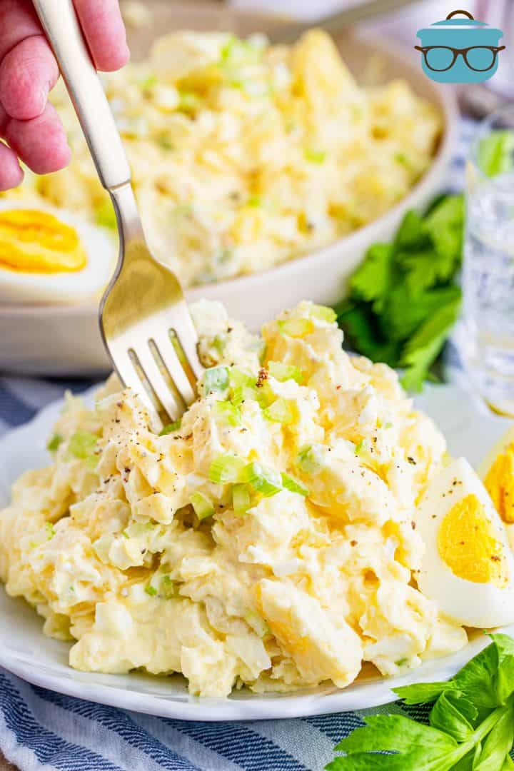 serving of potato salad on a small white plate with a fork sticking into it.