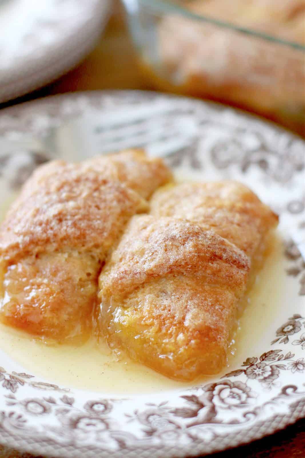 two apple cinnamon crescent roll dumplings on a brown and white plate