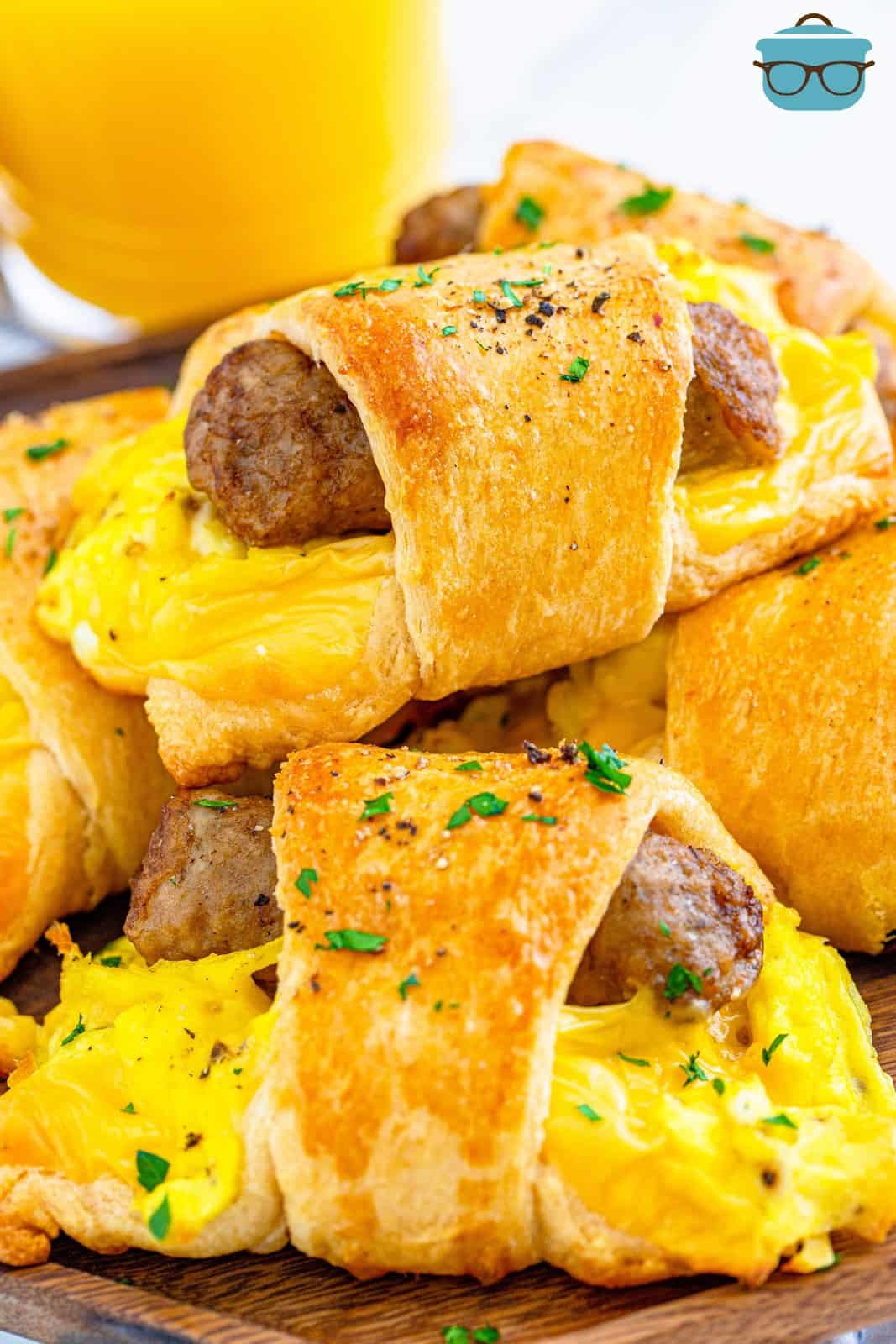 A stack of breakfast crescent rolls shown on a wooden serving plate with a glass of orange juice in the background. 