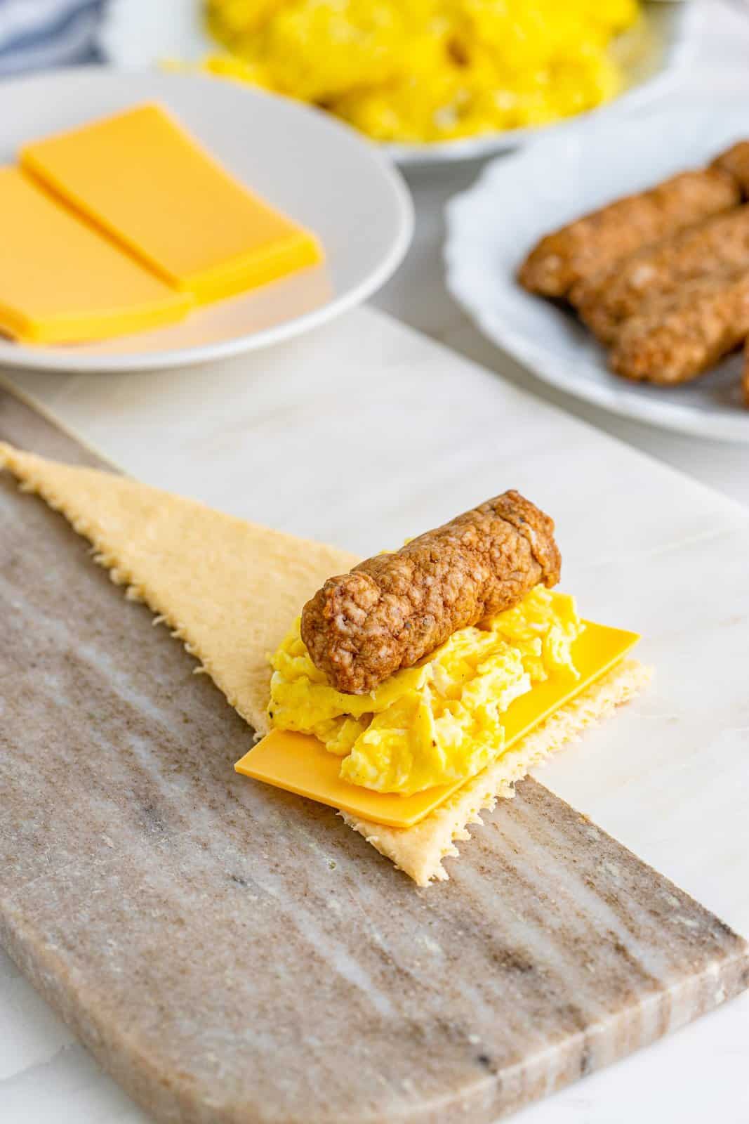 slice of cheese, scrambled eggs and a sausage link showed on one triangle shaped crescent roll. 