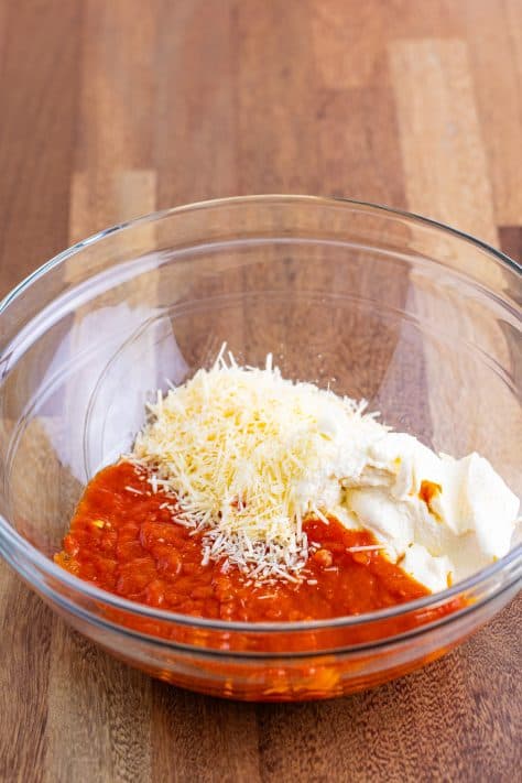 A mixing bowl with marinara sauce, ricotta cheese and parmesan cheese.