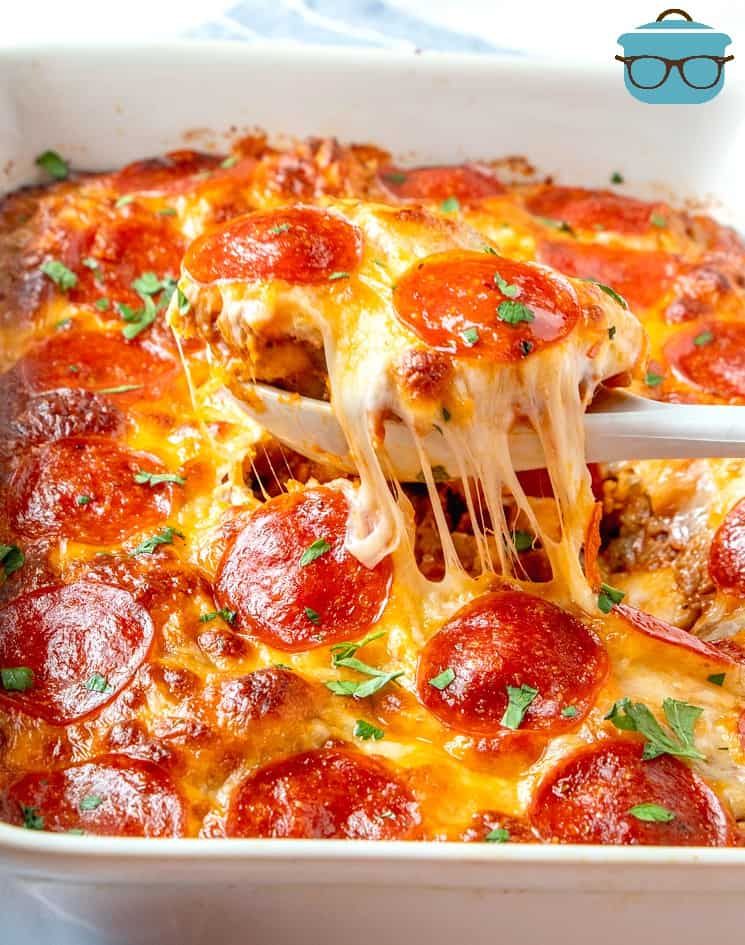 Bubble Up Pizza, finished, in a baking dish with a spoon pulling out a serving with melted cheese.